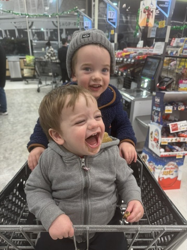 Two young children laughing together in a shopping cart.