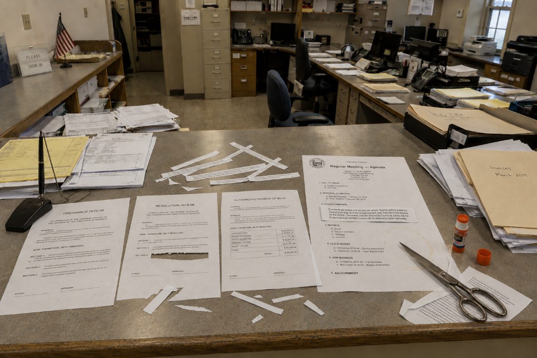 A council agenda being assembled by hand with scissors and glue on an office counter.