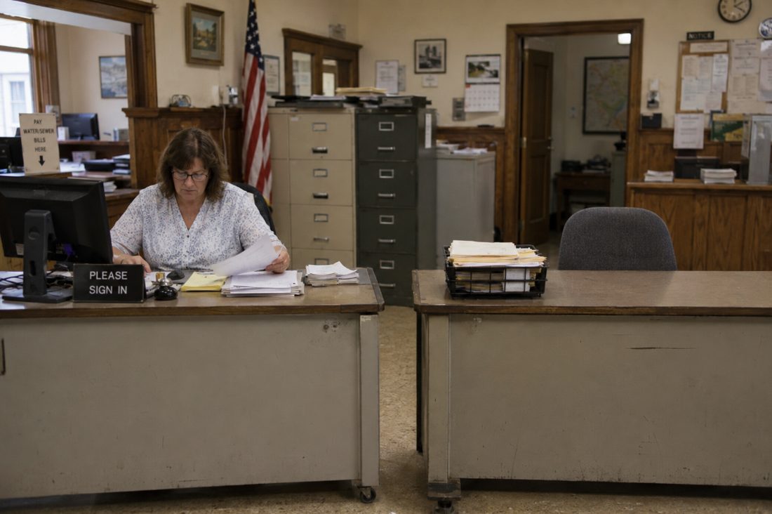 A municipal clerk works the counter of a busy town hall office.